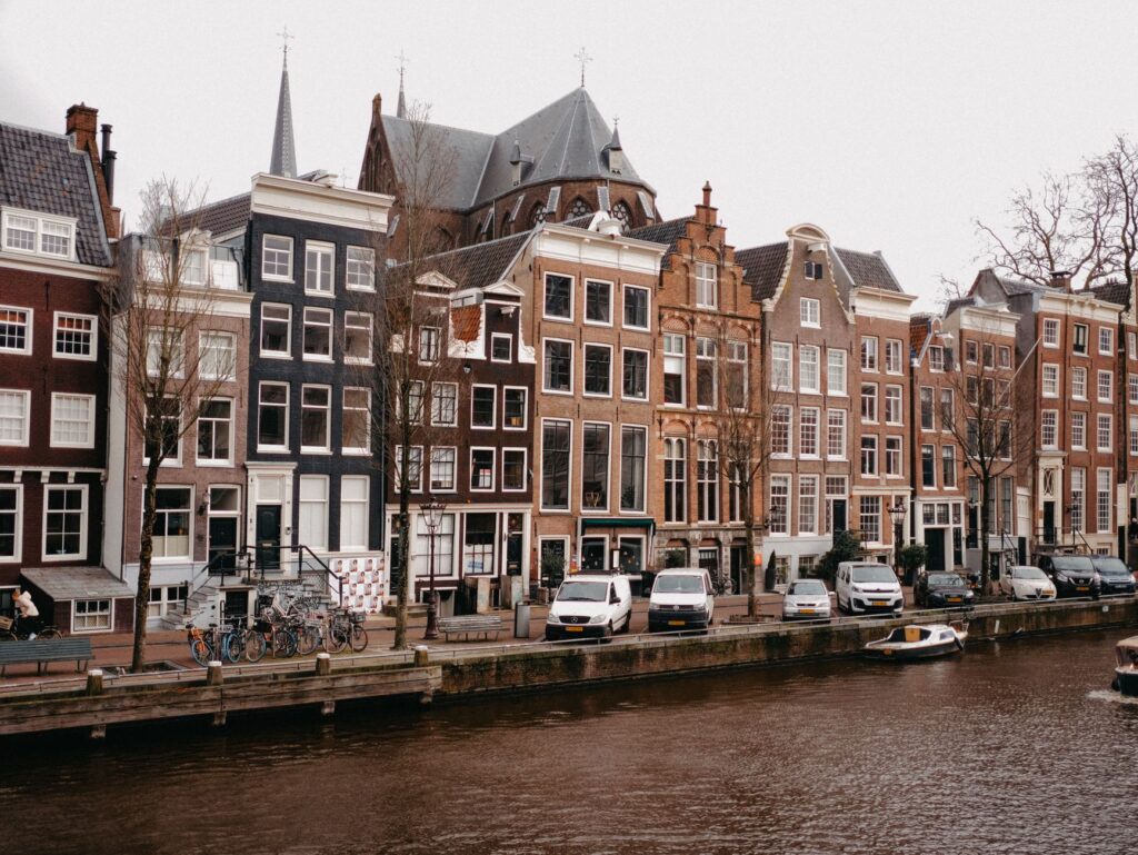 Scenic view of Amsterdam's iconic canal and traditional Dutch row houses with canal boats and cars lined up.