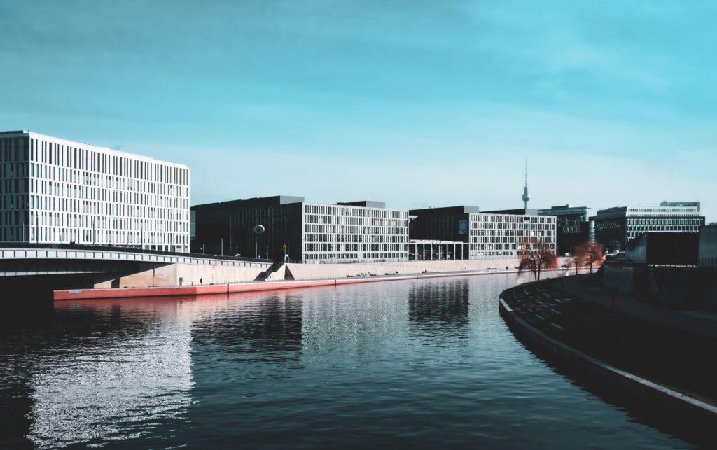 Contemporary buildings line the river in Berlin under a clear sky.