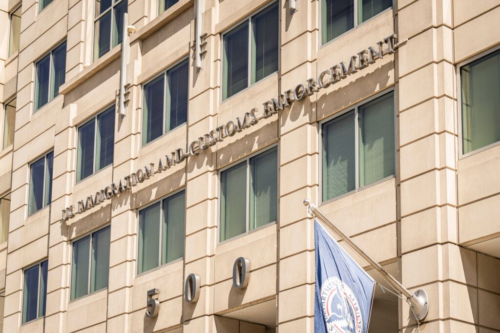 Exterior view of the US Immigration and Customs Enforcement building with a visible flag and signage.