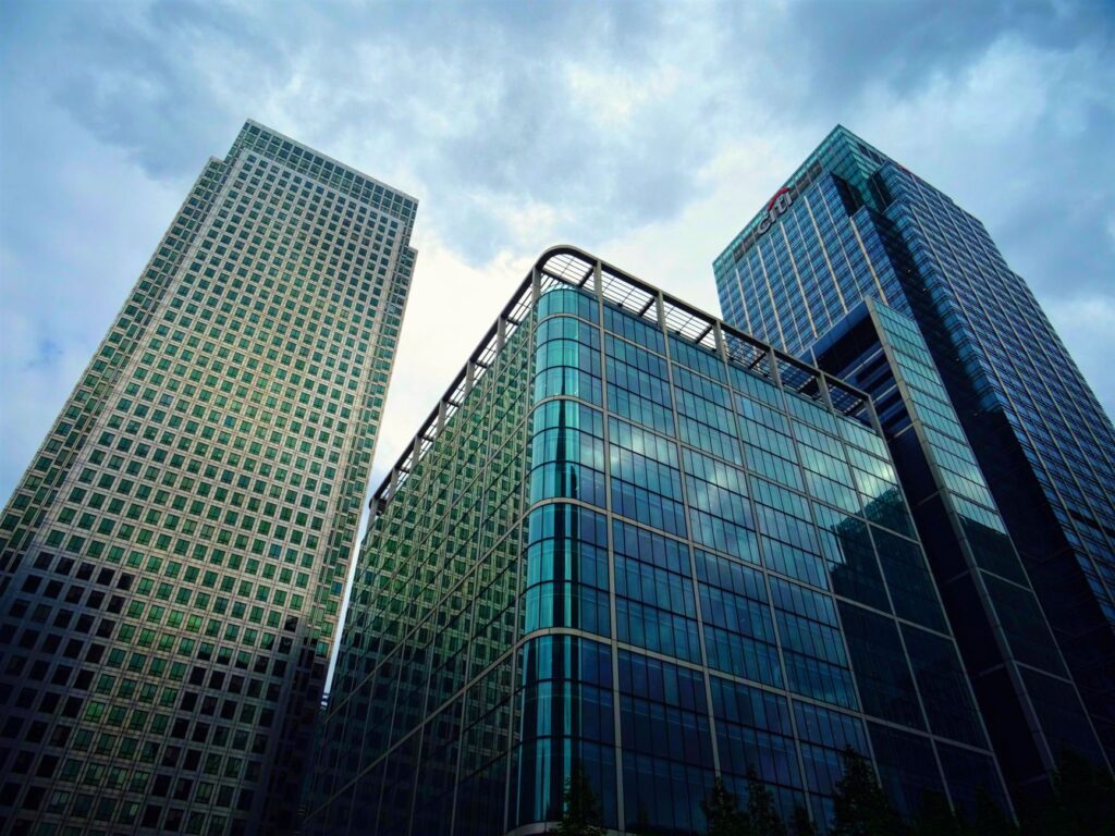 Low angle view of modern skyscrapers with glass facades and cloudy sky backdrop in city downtown.