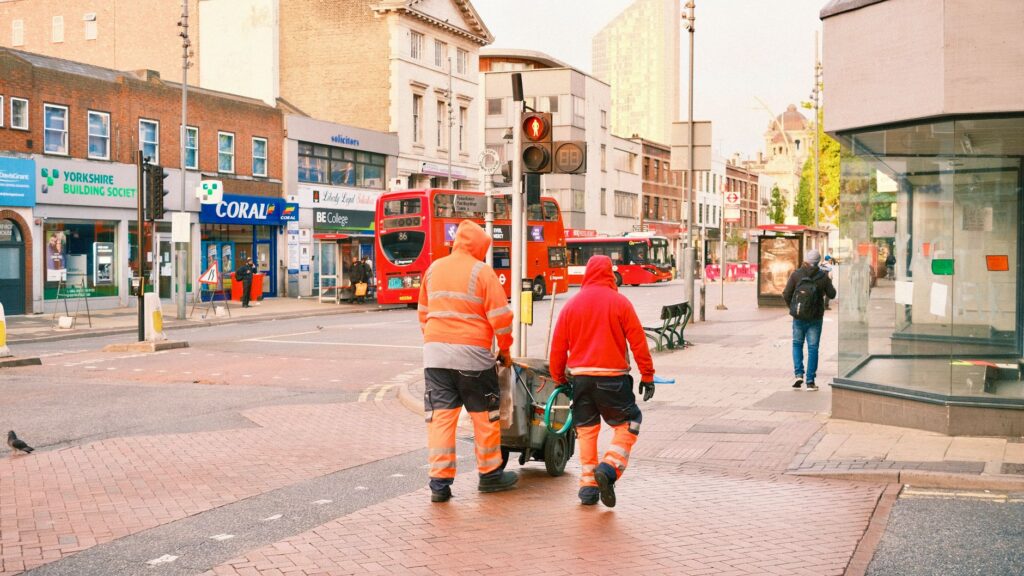 Busy city intersection with pedestrians, double decker buses, and workers.