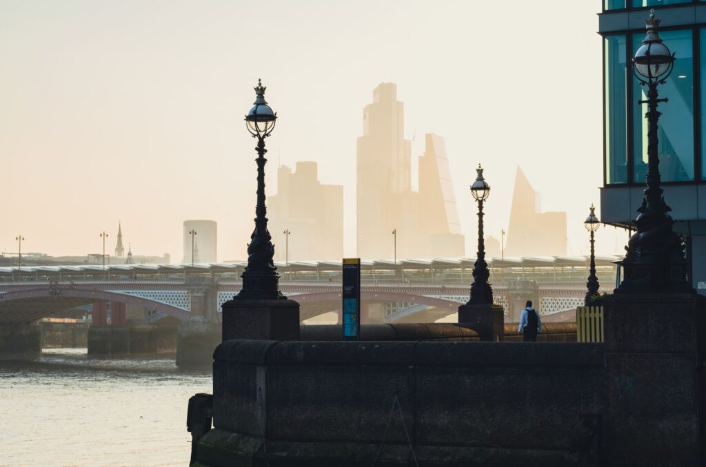 City skyline with river and bridge, featuring urban architecture and street lamps in foreground.