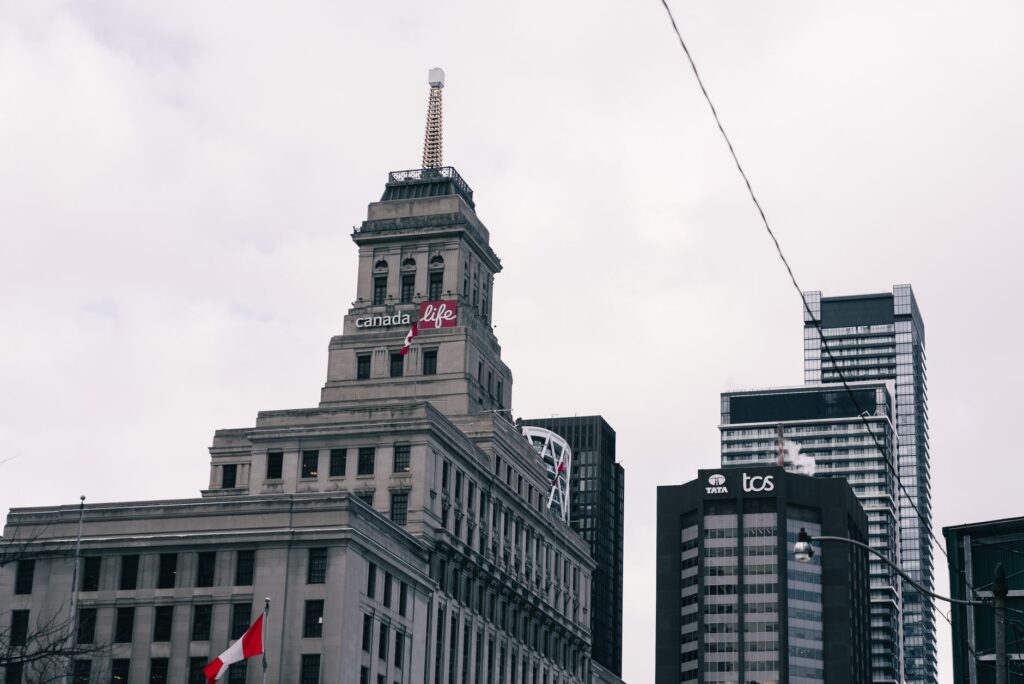 View of the Canada Life Building in Toronto with surrounding skyscrapers on a cloudy day.